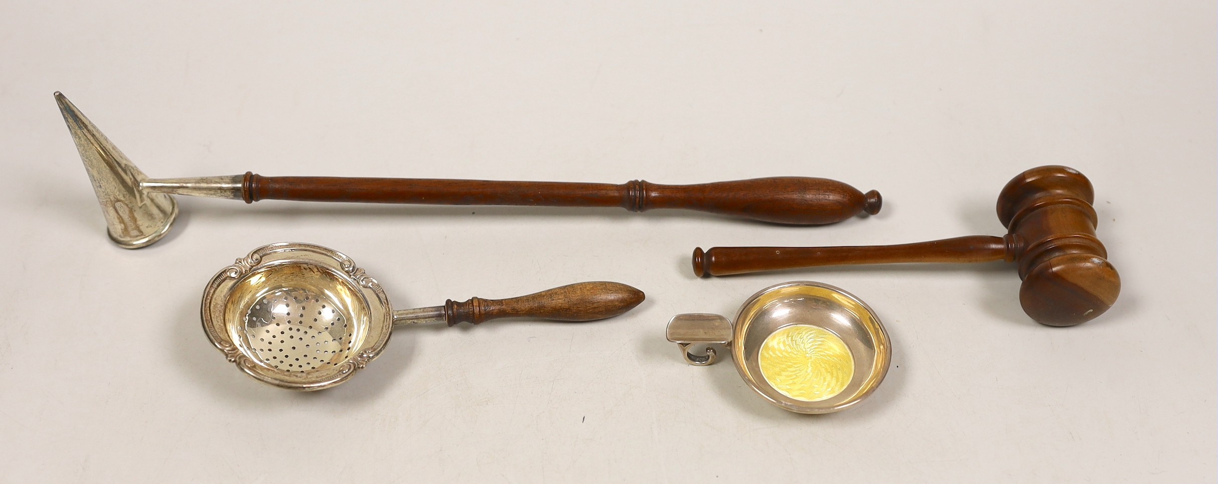 A George V silver extinguisher, with turned wooden handle, 30.8cm, a silver tea strainer, a silver and enamel ashtray and a wooden gavel.